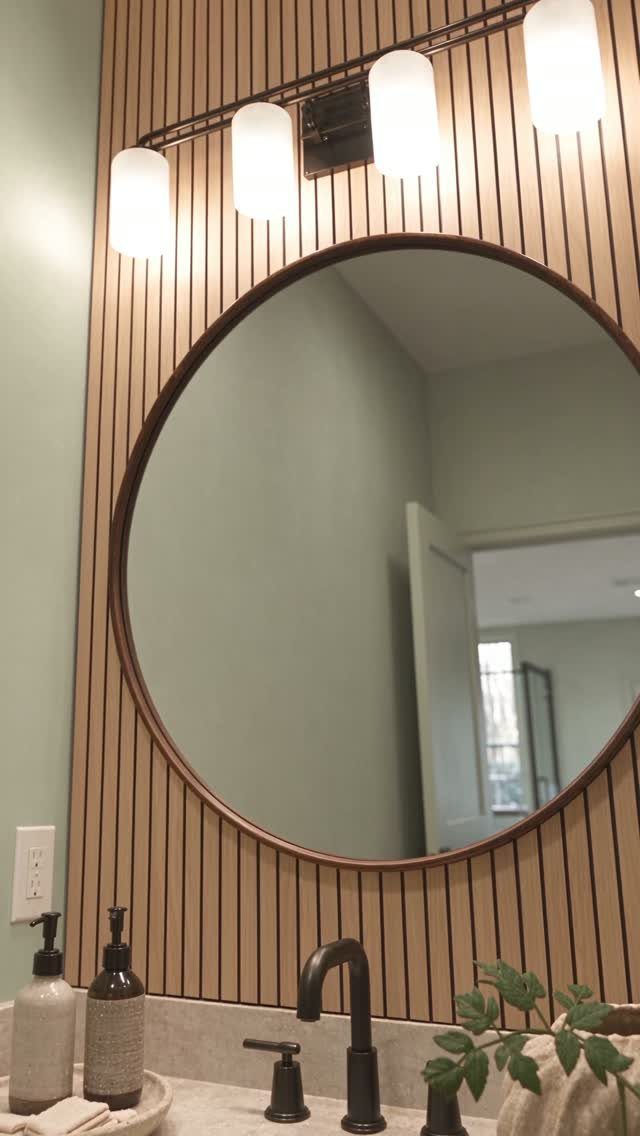 A round mirror mounted on a wall with vertical light wood slat paneling above a bathroom vanity.
