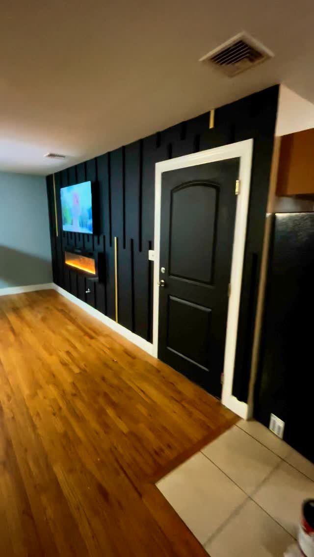 Black accent wall with vertical wood slats, gold accents, a television, and a fireplace.