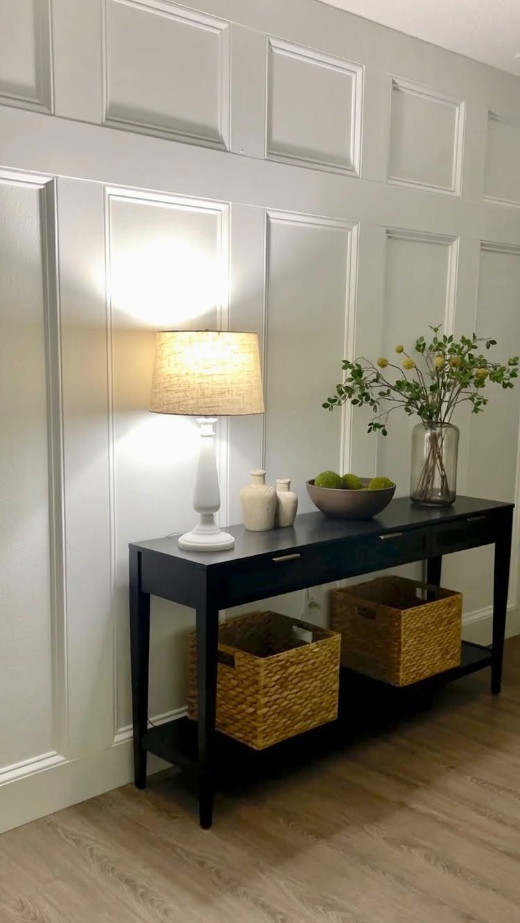 Light grey paneled wall with decorative molding behind a black console table and lamp.