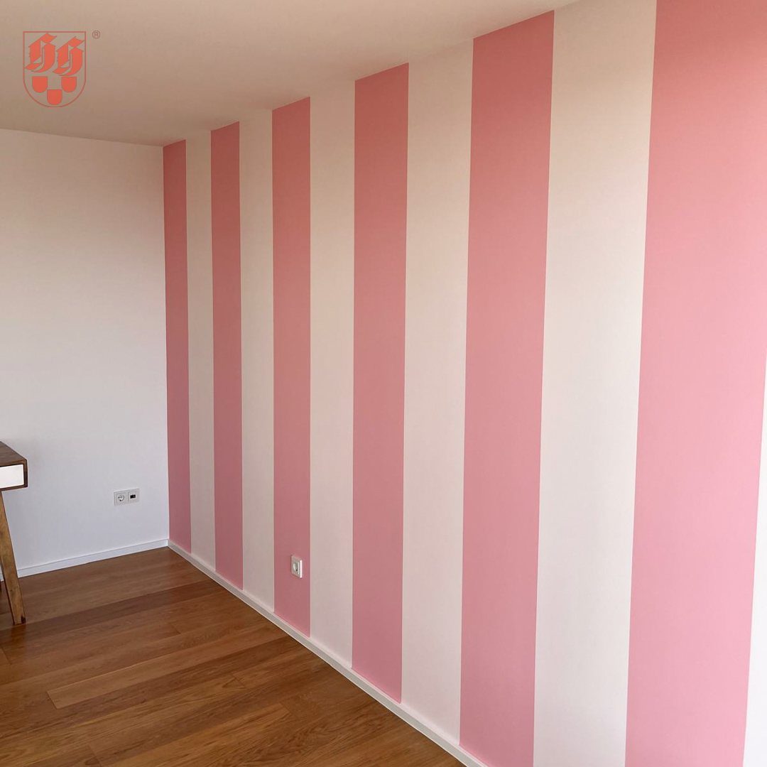 Vertical pastel pink and white stripes painted on an interior accent wall above wooden flooring.