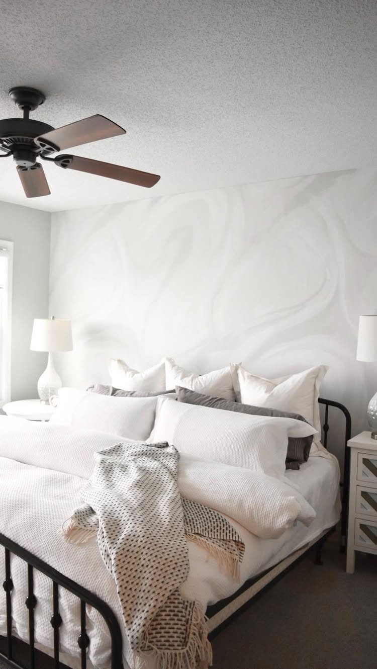 A bed with white bedding sits against a wall with grey swirling wallpaper.