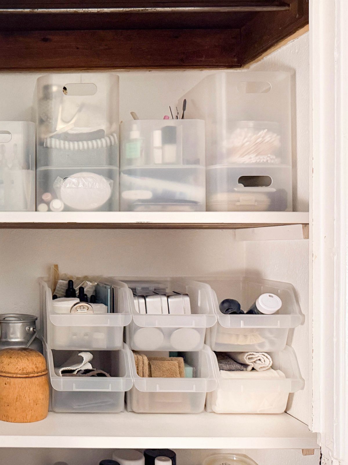 14 Bathroom Small Space Storage Ideas That Actually Fit 2 Translucent plastic storage bins filled with toiletries and towels sit on white shelves.