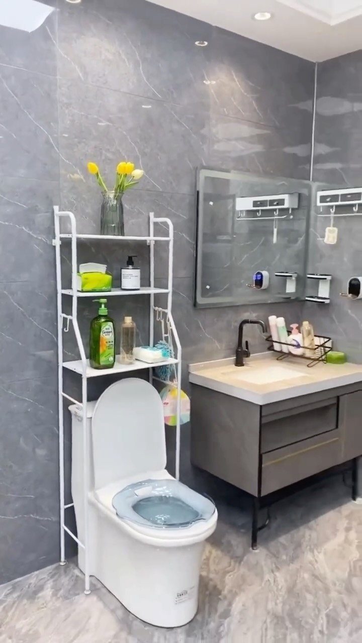 14 Bathroom Small Space Storage Ideas That Actually Fit 1 White metal shelving unit holding toiletries and flowers positioned above a white toilet in a grey bathroom.