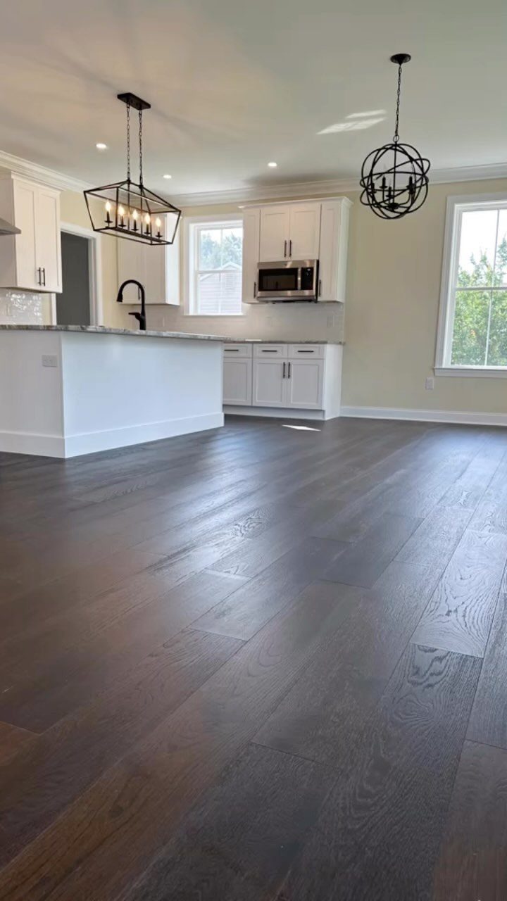 Dark stained hardwood floors in a bright, modern kitchen with white cabinets and black lighting fixtures.