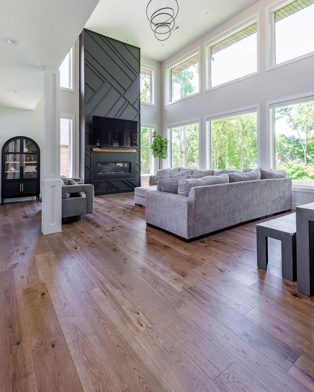 Medium-toned hardwood planks stretching across a bright, modern living room with large windows.