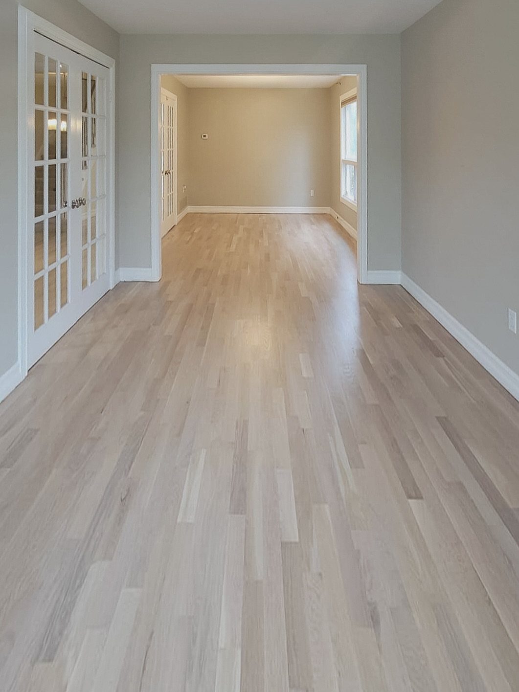 Light whitewashed hardwood floors extending through an empty room with neutral walls and white trim.