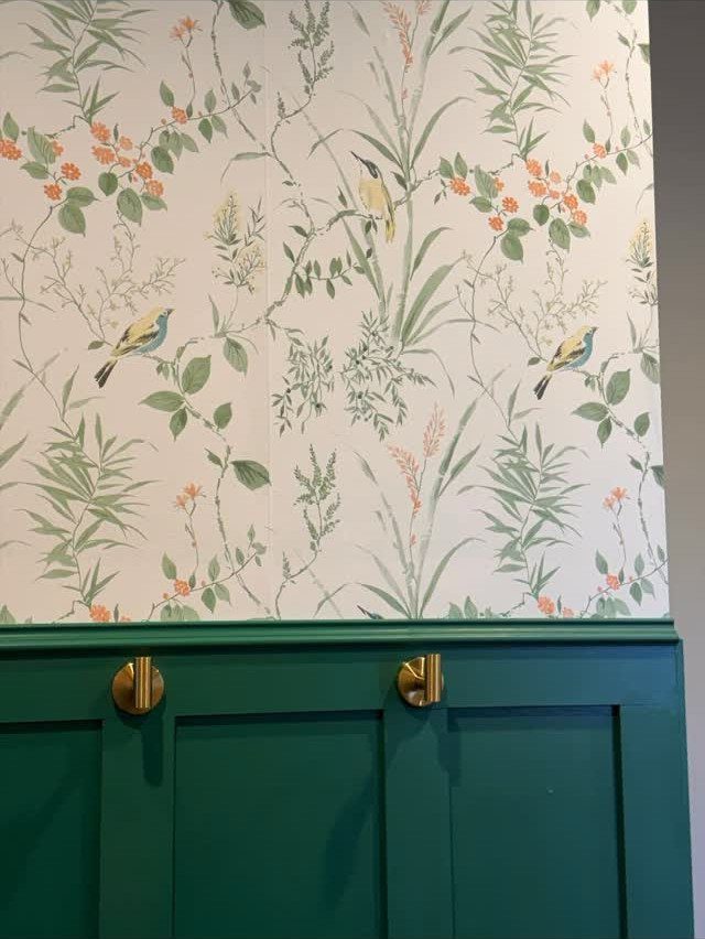 Botanical patterned wallpaper above dark green board and batten wall with gold knobs.