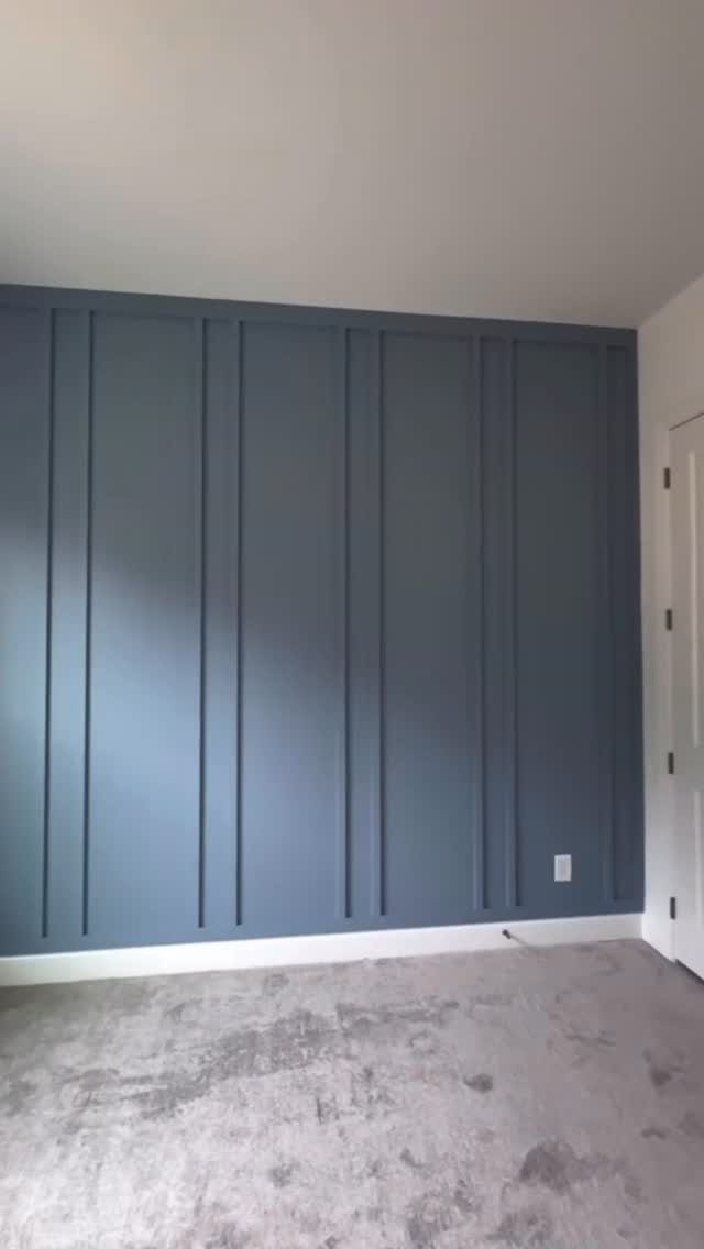 Blue accent wall with vertical board and batten molding and grey carpeted floor.