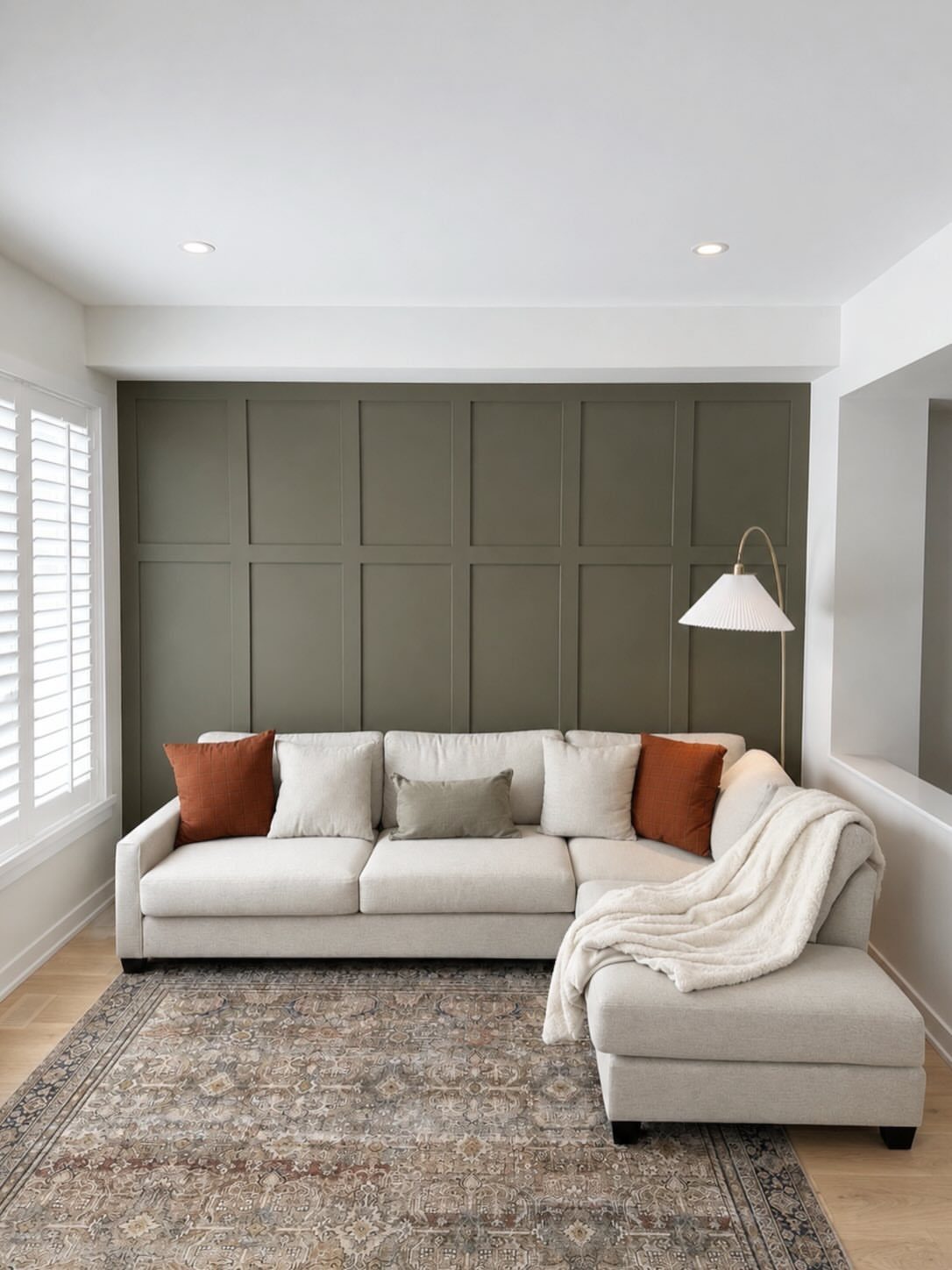 Olive green board and batten accent wall behind a beige sectional sofa and patterned rug.