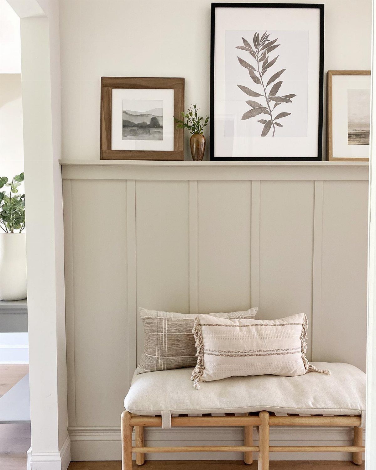 Beige board and batten wainscoting wall with a wooden bench and decorative pillows.