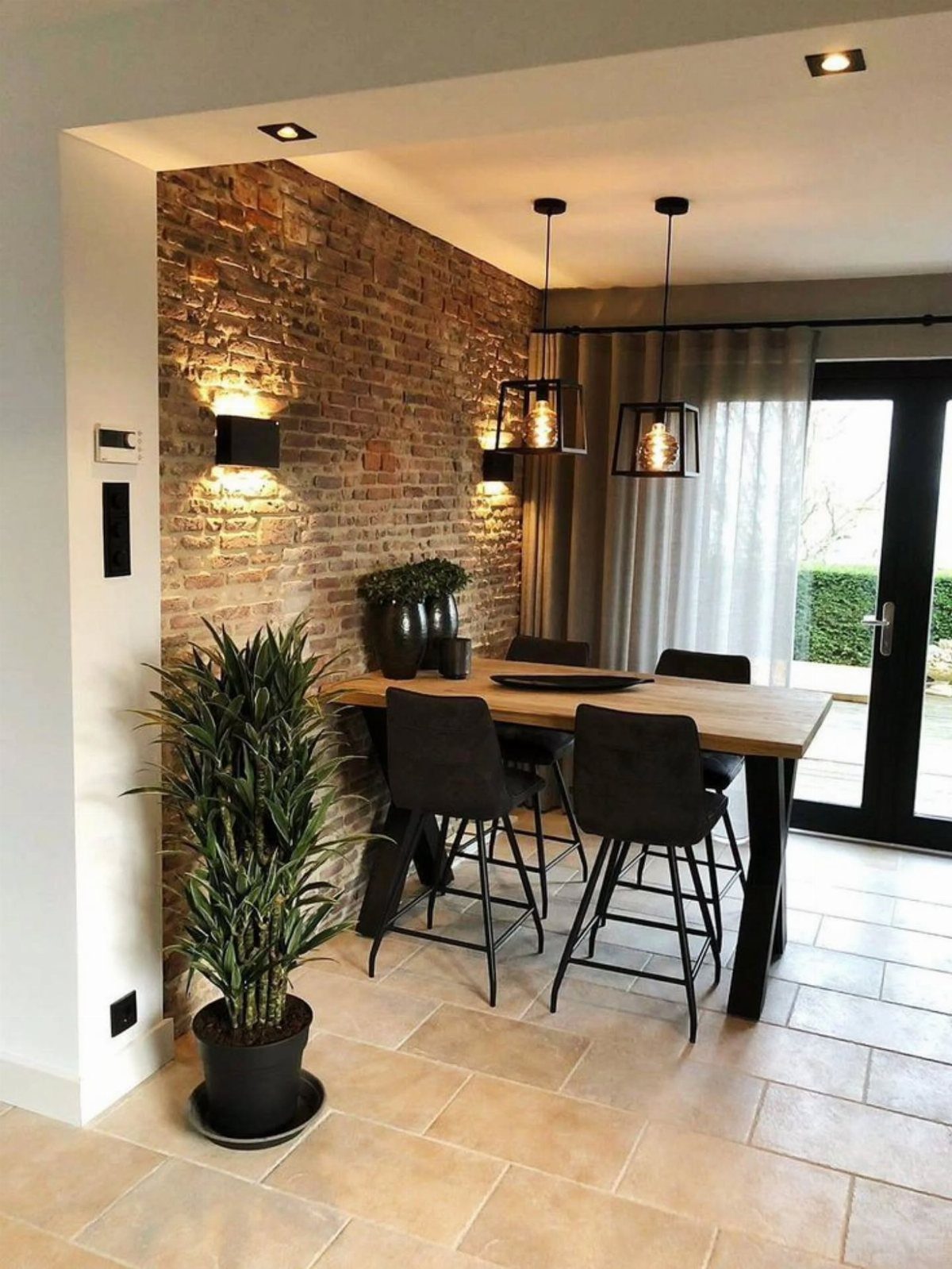 A wooden dining table and black chairs set against a rustic brown brick accent wall.