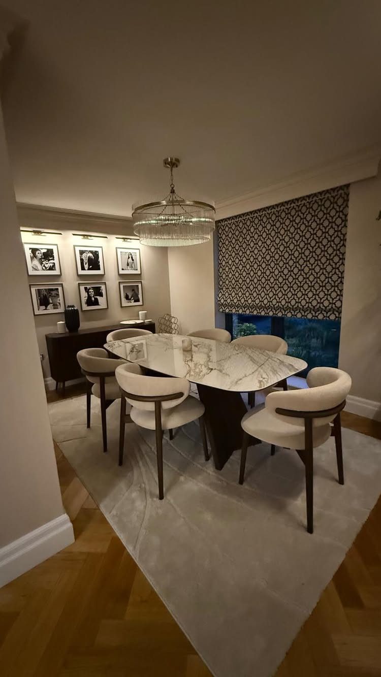 Dining room with marble table, cream chairs, crystal chandelier, and a gallery wall of framed photos.