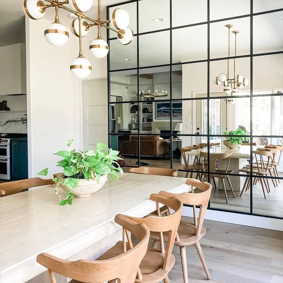A dining table with wooden chairs set against a large black-framed mirror accent wall.