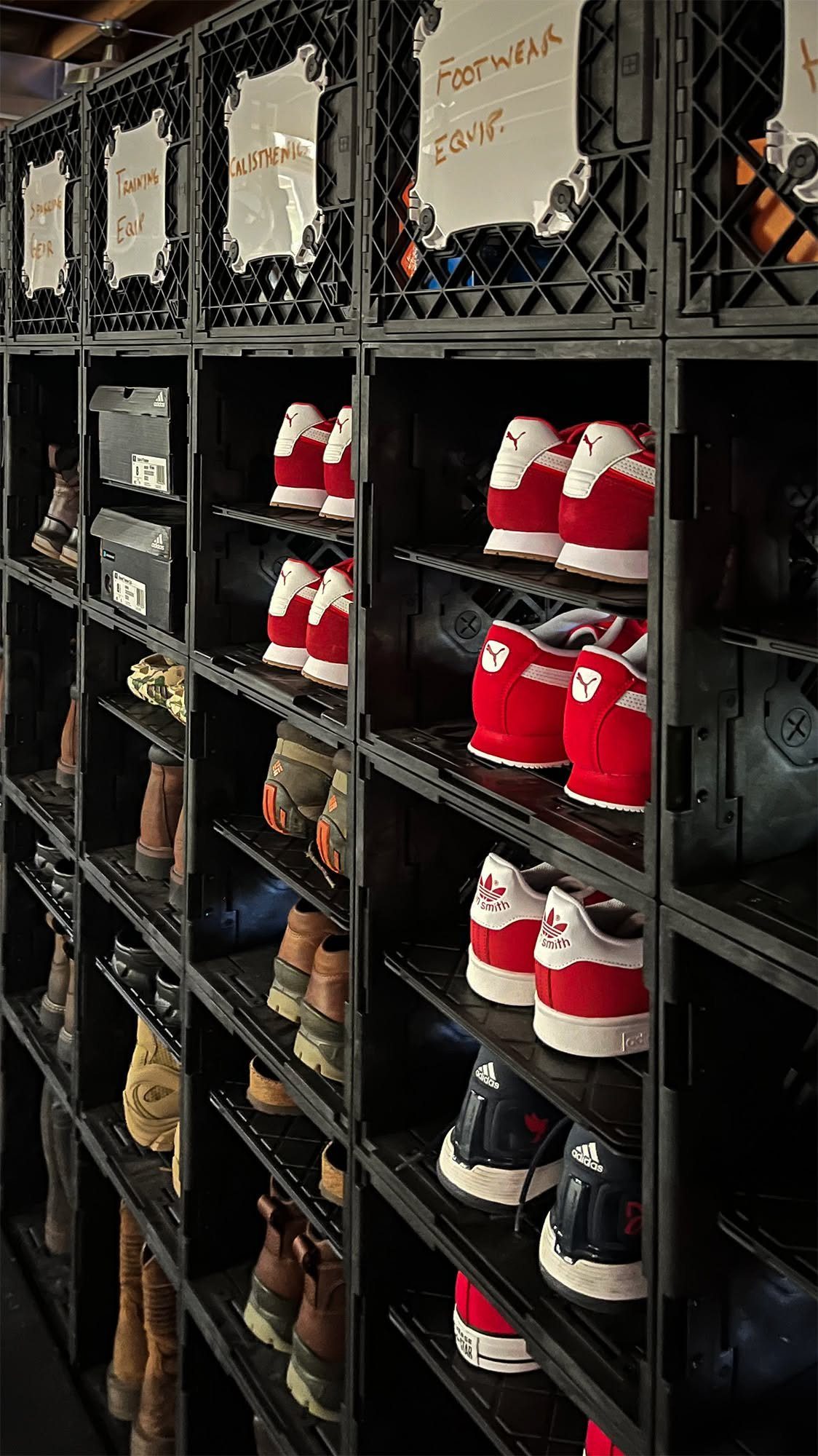 Black plastic milk crates stacked in a grid containing various pairs of colorful sneakers.