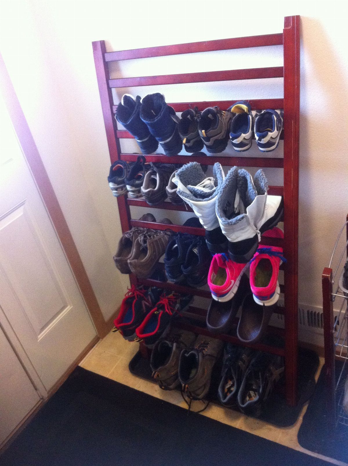 A wooden slatted rack holding various pairs of shoes against a white wall.