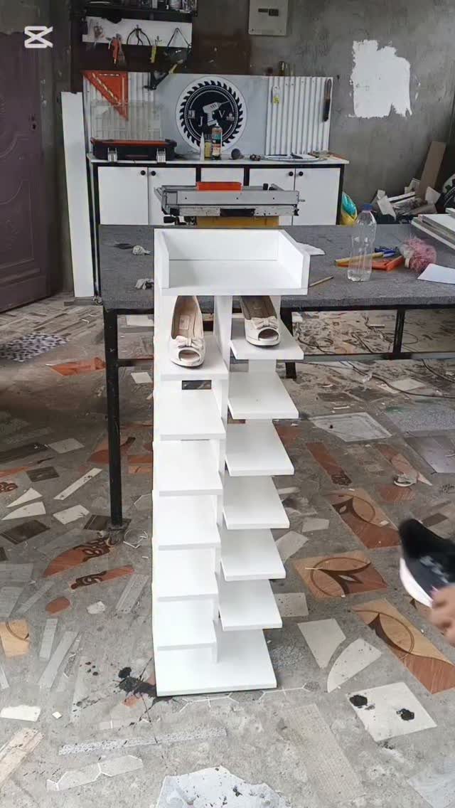 A white vertical shoe rack with staggered shelves holding two pairs of shoes in a workshop.