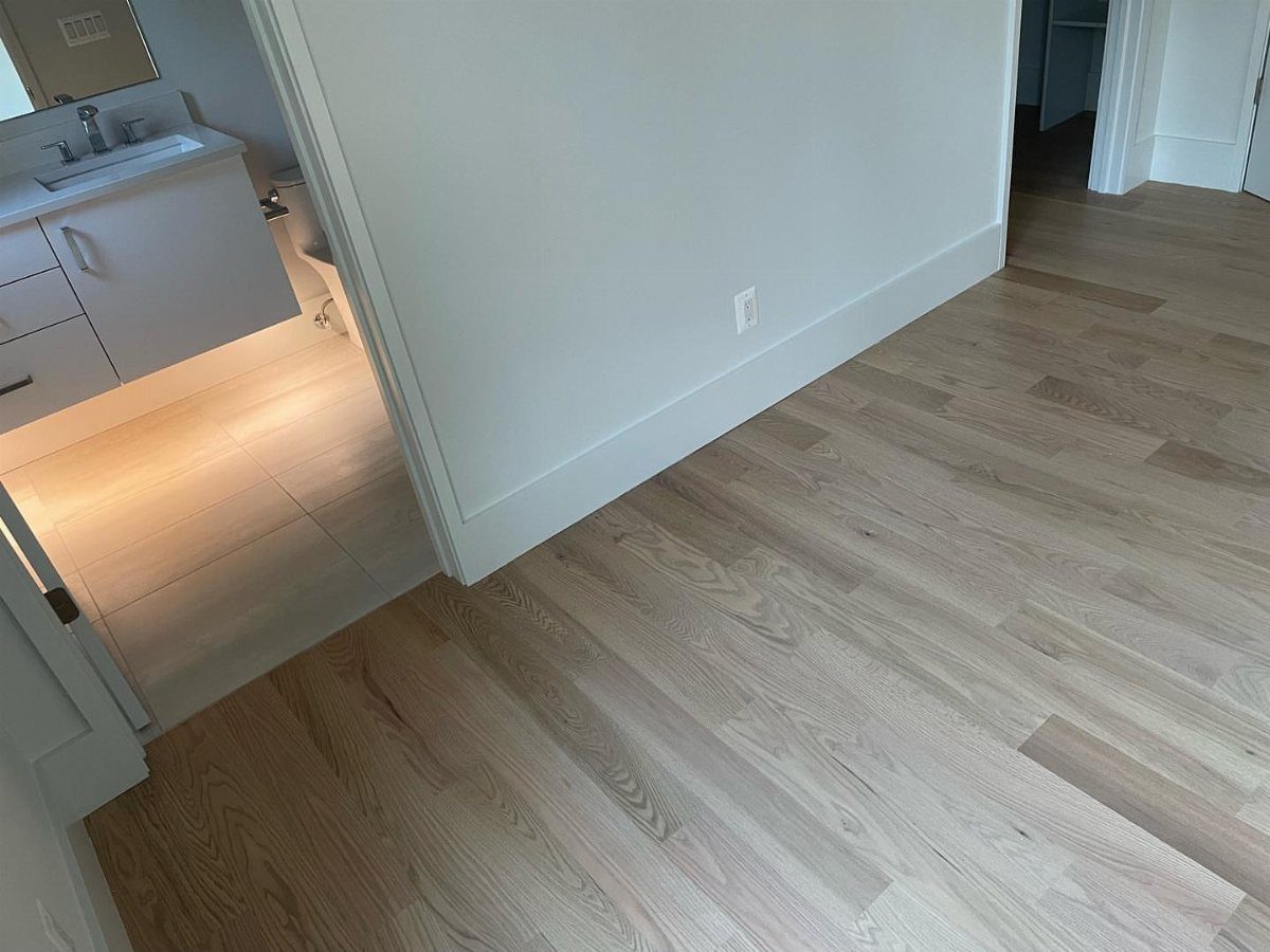 Light wood flooring with visible grain patterns running through a hallway and into a bathroom.