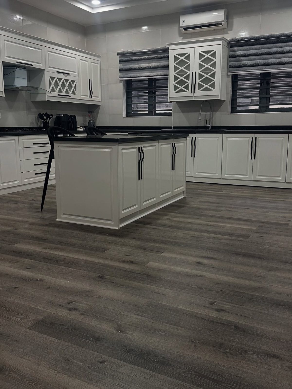 Grey wood-look plank flooring in a modern kitchen with white cabinets and black countertops.