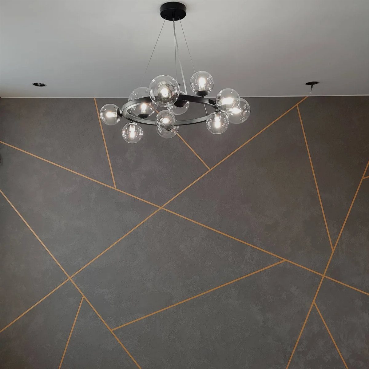 Dark grey wall with intersecting gold geometric lines and a modern glass globe chandelier.