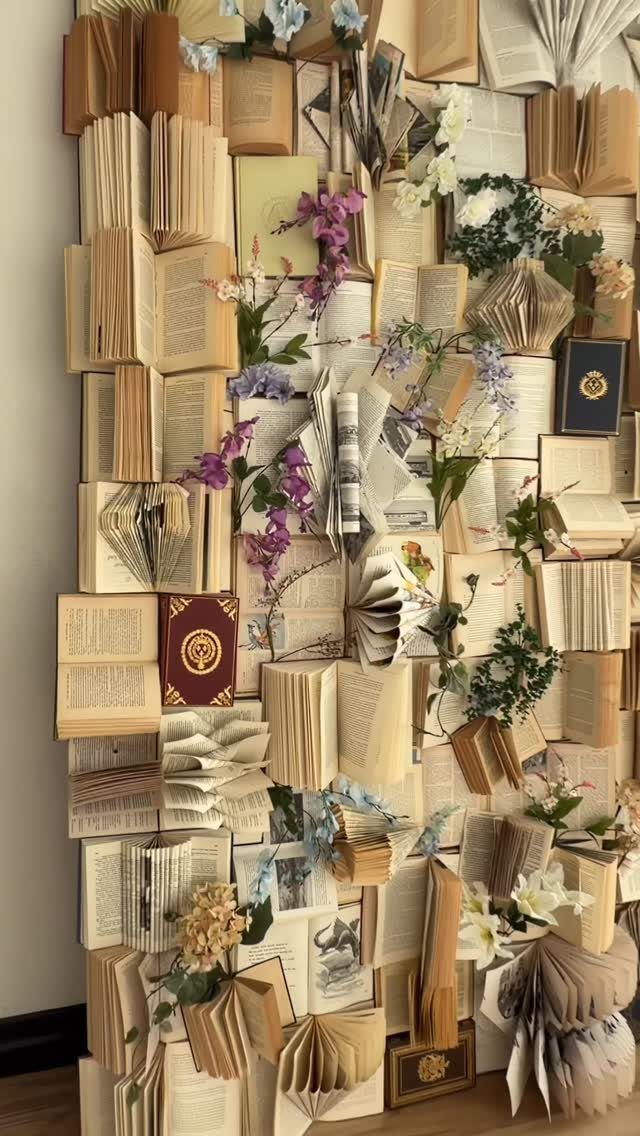Open and closed books arranged on a wall with decorative flowers and greenery.