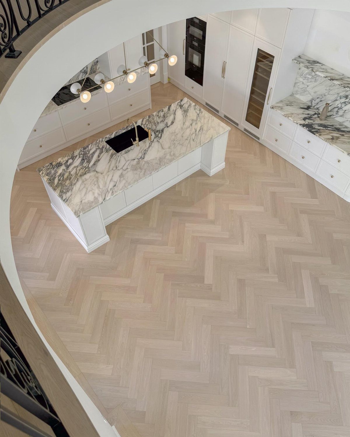 11 Kitchen Flooring Trends for 2026 That Actually Hold Up 1 Light wood herringbone pattern flooring in a modern white kitchen with a marble island.