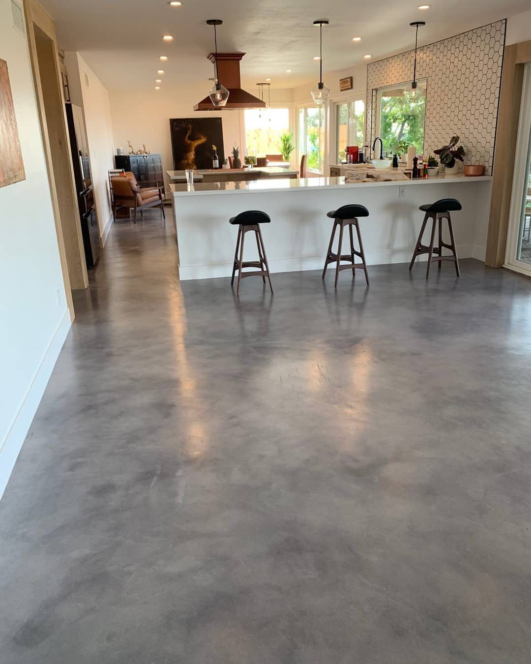 11 Kitchen Flooring Trends for 2026 That Actually Hold Up 8 Polished gray concrete flooring in a modern kitchen with a white island and bar stools.