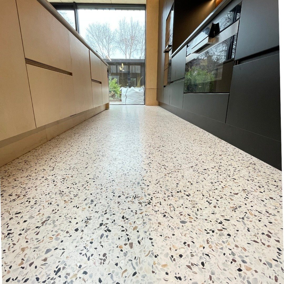 11 Kitchen Flooring Trends for 2026 That Actually Hold Up 5 Terrazzo tiles with multicolored stone chips covering a modern kitchen floor between sleek cabinets.