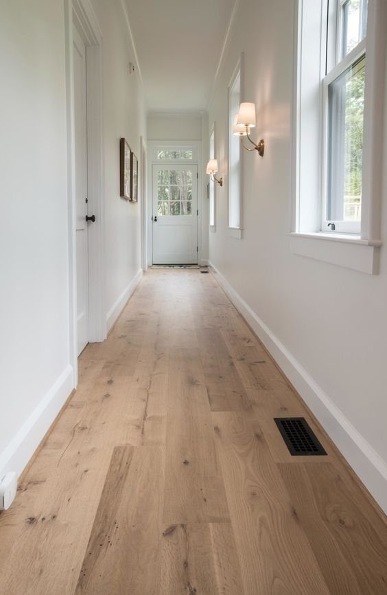 Light oak wood flooring running through a bright, white hallway towards a door.