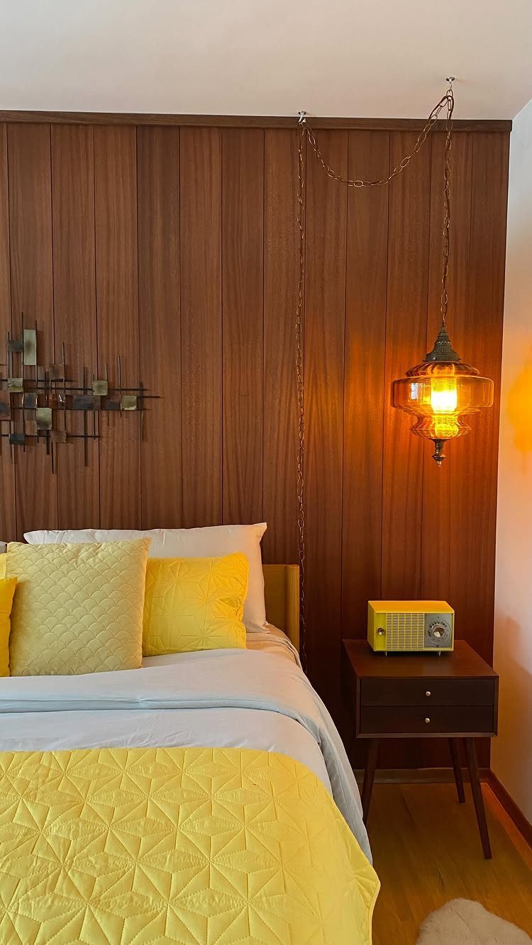 Vertical wood paneling covers a bedroom wall behind a bed with yellow pillows and bedding.