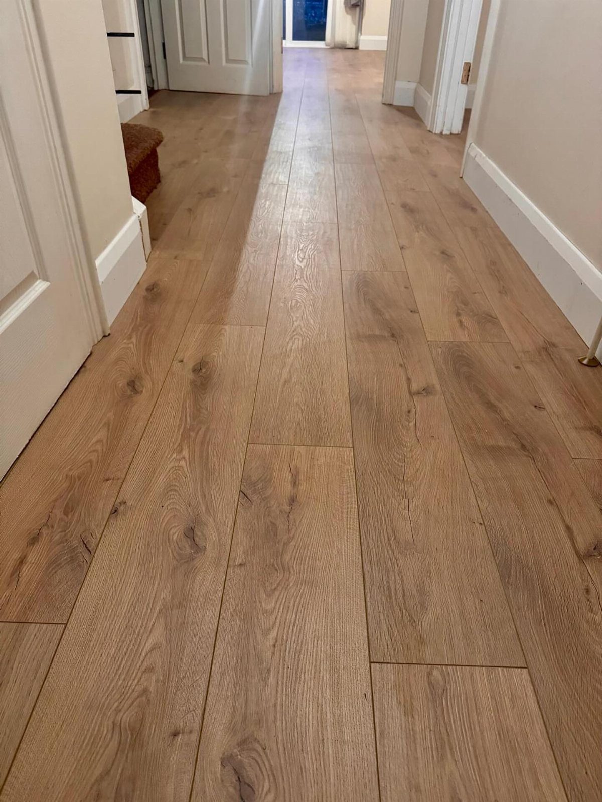 Light brown wood-look planks installed as flooring in a hallway between white walls.