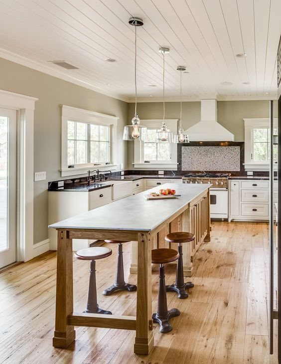 A narrow wooden kitchen island with a white countertop and four backless stools on light wood floors.