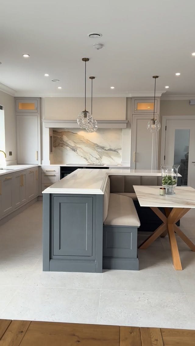 Grey kitchen island featuring a built-in upholstered bench seat and white marble countertop.