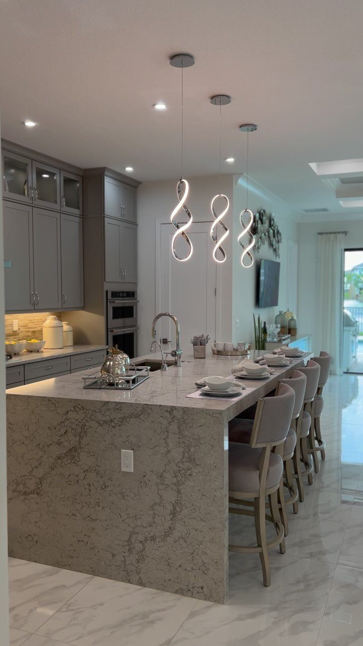 Three spiral-shaped pendant lights hanging over a large grey marble kitchen island with upholstered stools.