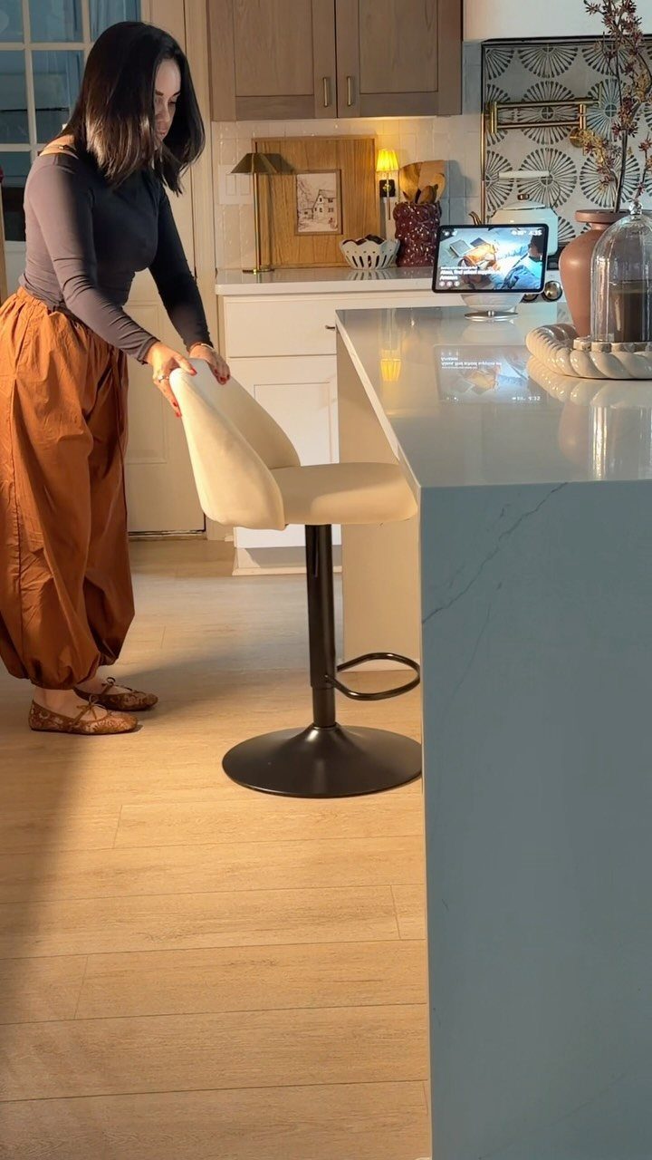 A woman adjusts a cream upholstered swivel bar stool next to a white kitchen island.