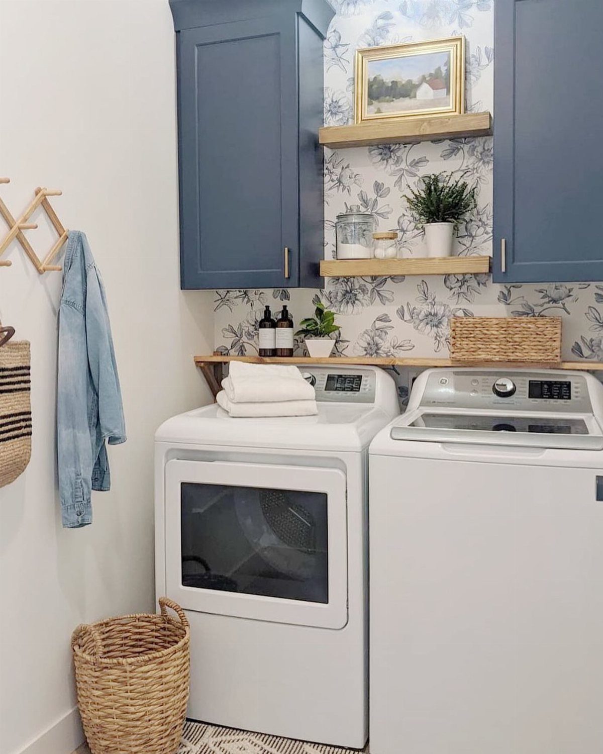 10 Small Laundry Closet Ideas That Actually Fit in a Hallway 3 White washer and dryer set against blue floral wallpaper and blue cabinets in a laundry closet.