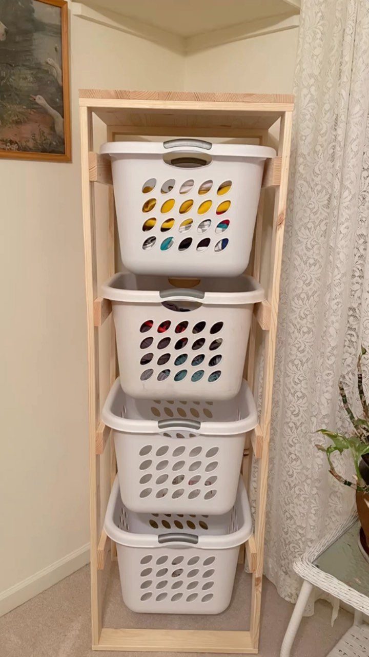 10 Small Laundry Closet Ideas That Actually Fit in a Hallway 10 Four white plastic laundry baskets stacked vertically inside a light wooden frame structure.