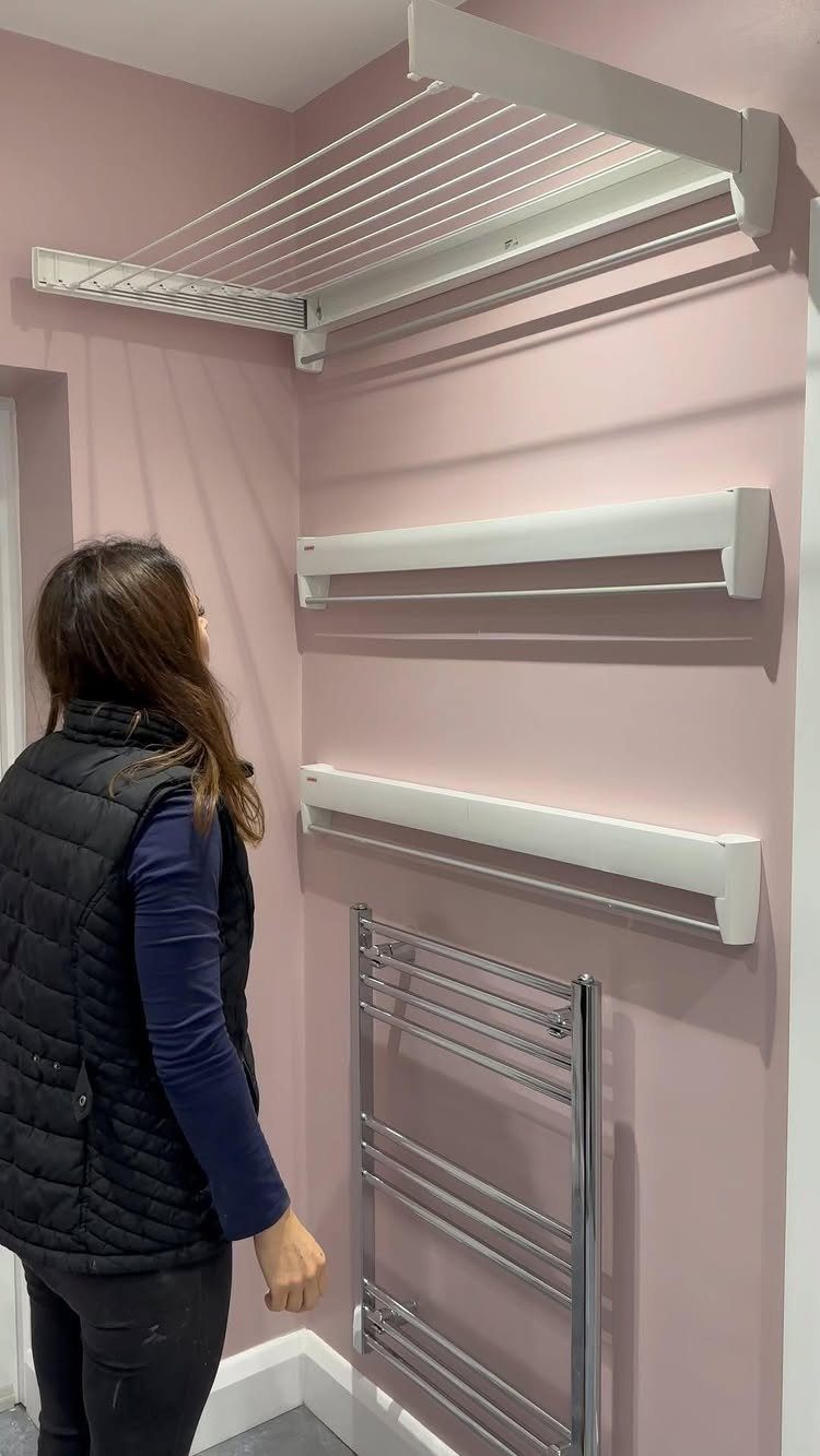 10 Small Laundry Closet Ideas That Actually Fit in a Hallway 7 A woman looks at a white wall-mounted drying rack installed in a pink laundry room.