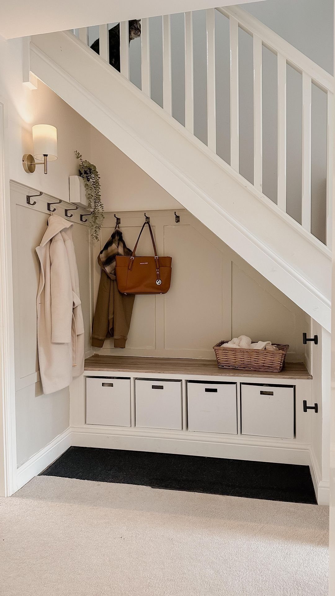 7 Stairs with Under Storage Ideas That Actually Work 4 White under-stair storage nook with hanging coats, a handbag, and four white storage bins.