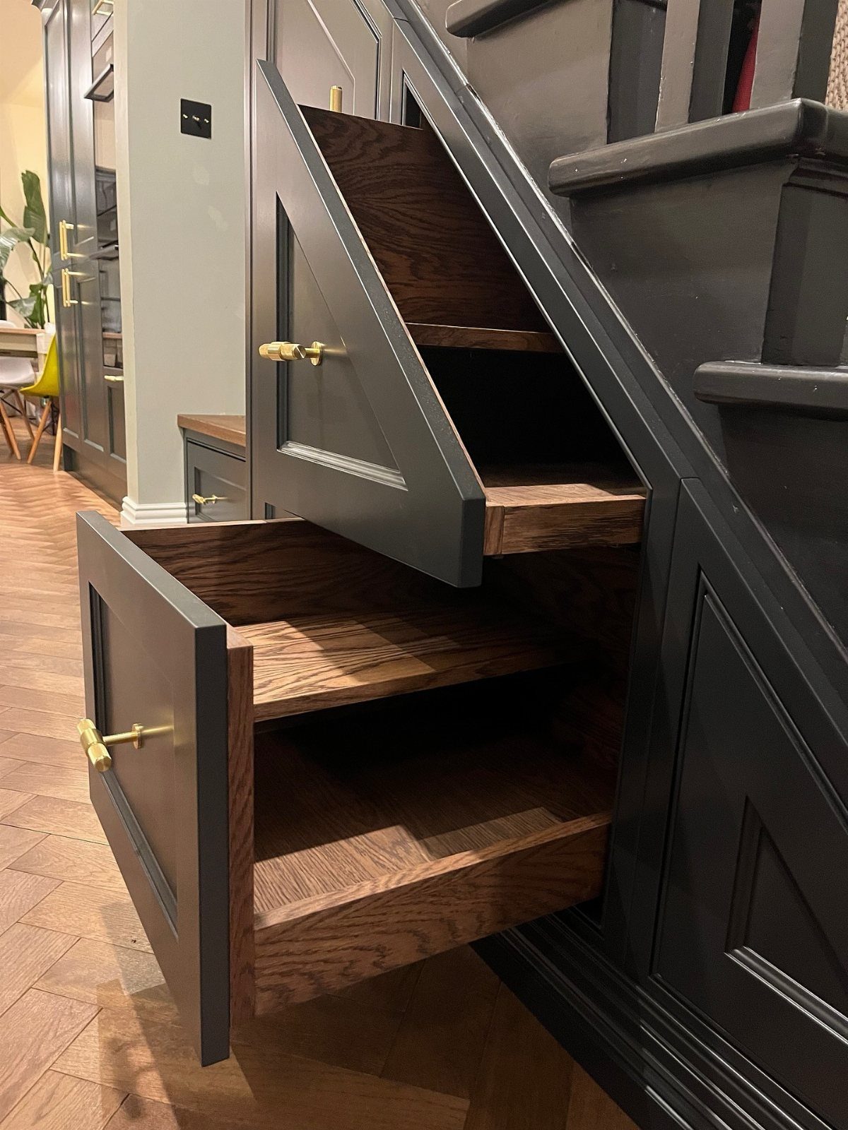 7 Stairs with Under Storage Ideas That Actually Work 2 Two large pull-out wooden drawers with dark grey fronts extended from under a staircase.