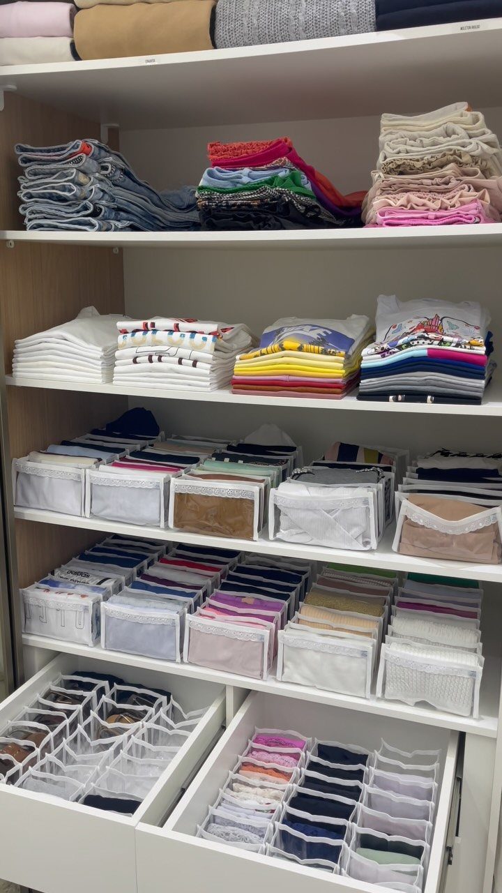 8 Storage Closet Organization Ideas for Tighter Spaces 2026 1 Folded stacks of colorful clothing and organized mesh storage bins on white closet shelves.