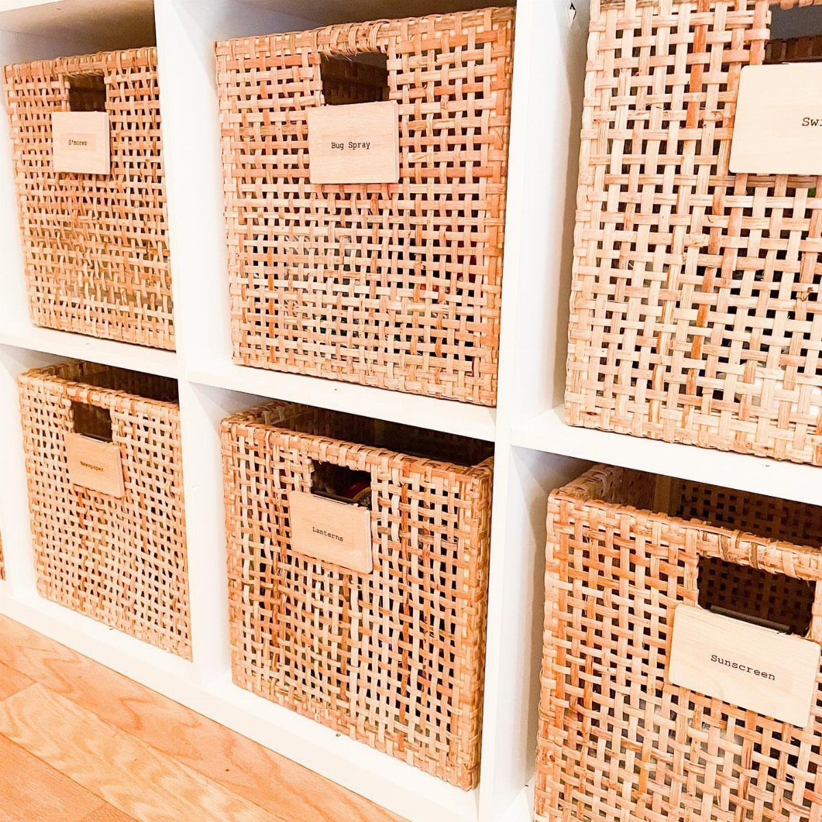 8 Storage Closet Organization Ideas for Tighter Spaces 2026 4 Woven wicker baskets with labels sit inside white cube storage shelves on a wooden floor.