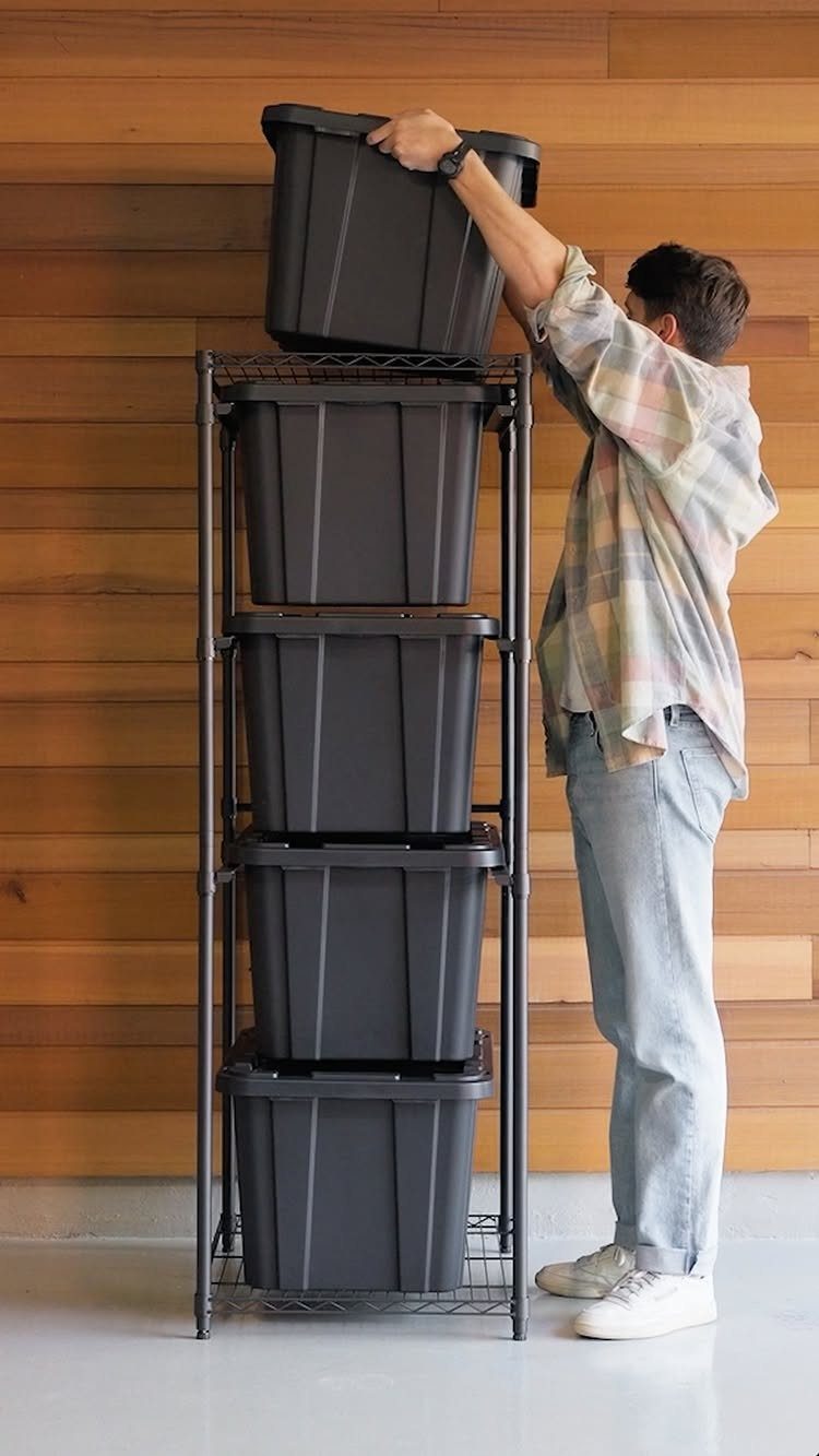 8 Storage Closet Organization Ideas for Tighter Spaces 2026 2 A man placing a large black plastic storage bin onto a tall metal shelving unit.