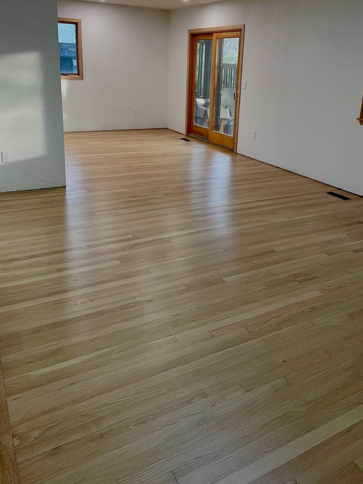 Light natural oak hardwood flooring installed in a spacious, empty room with white walls.