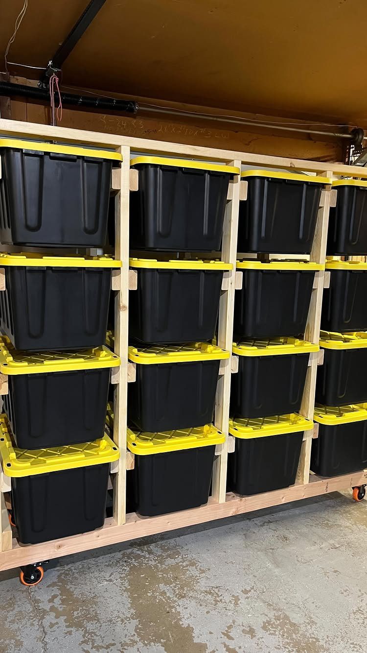 Black storage bins with yellow lids organized on a wooden rolling shelf unit.