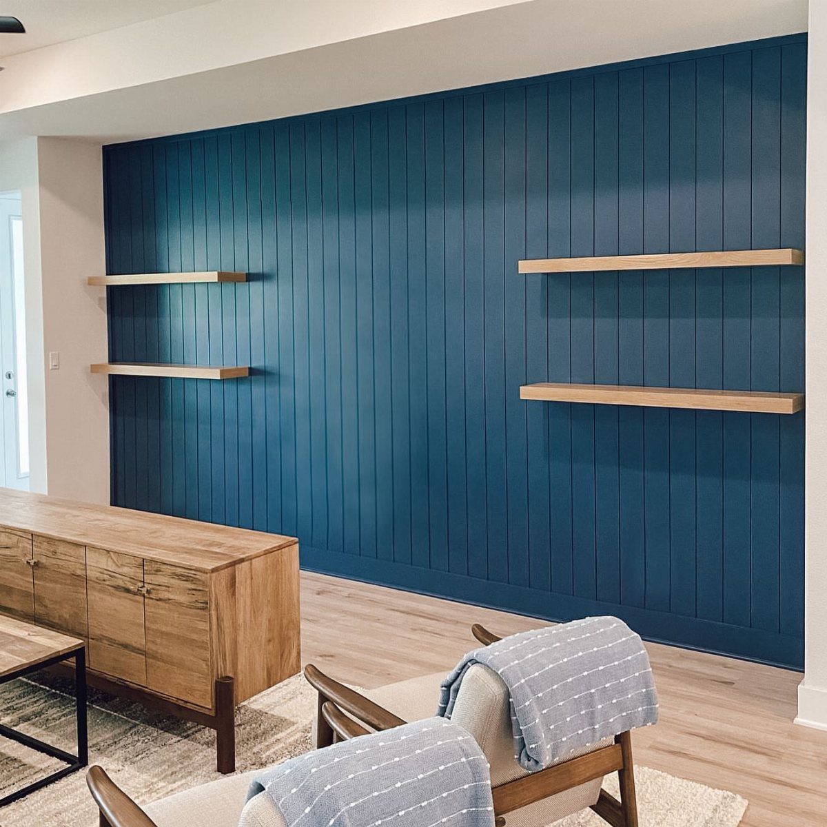 Deep teal vertical shiplap wall with two light wood floating shelves in a modern living room.