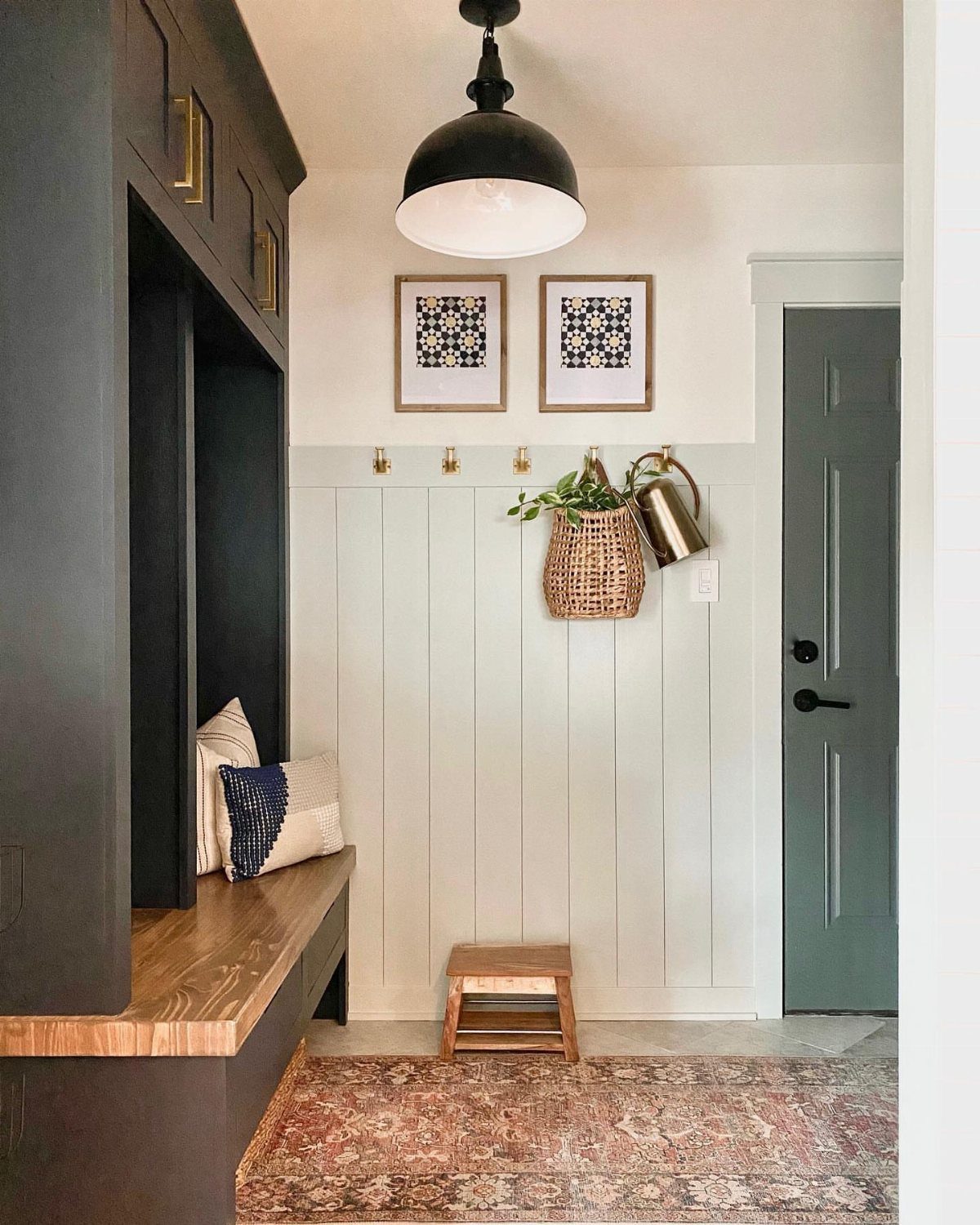 White vertical shiplap wall in a mudroom with gold hooks and a dark built-in bench.