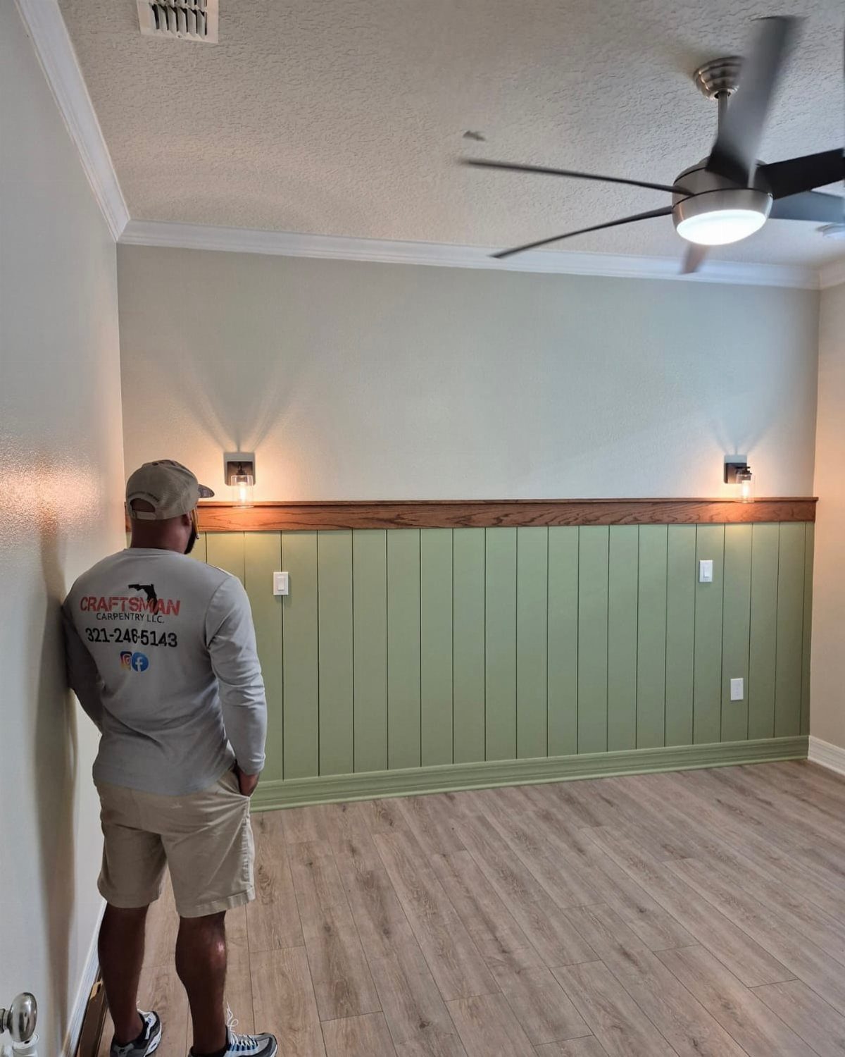 A man stands in a room looking at a sage green vertical shiplap wainscoting wall.