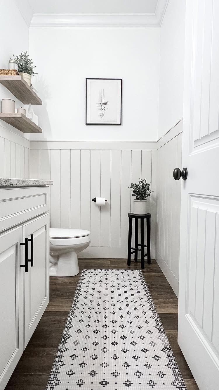 White vertical shiplap wainscoting in a small bathroom with a toilet and patterned rug.