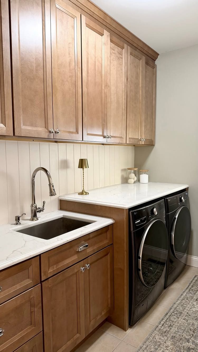 White vertical shiplap backsplash in a laundry room with wooden cabinets and black appliances.