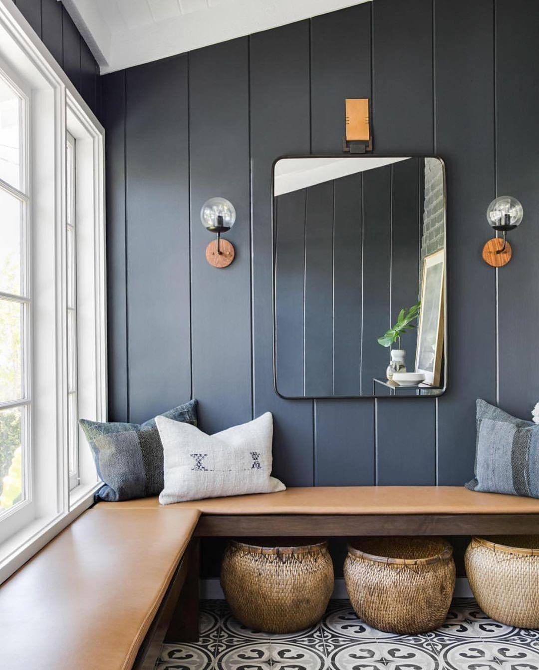 Dark charcoal vertical shiplap wall above a wooden bench with pillows and woven baskets.